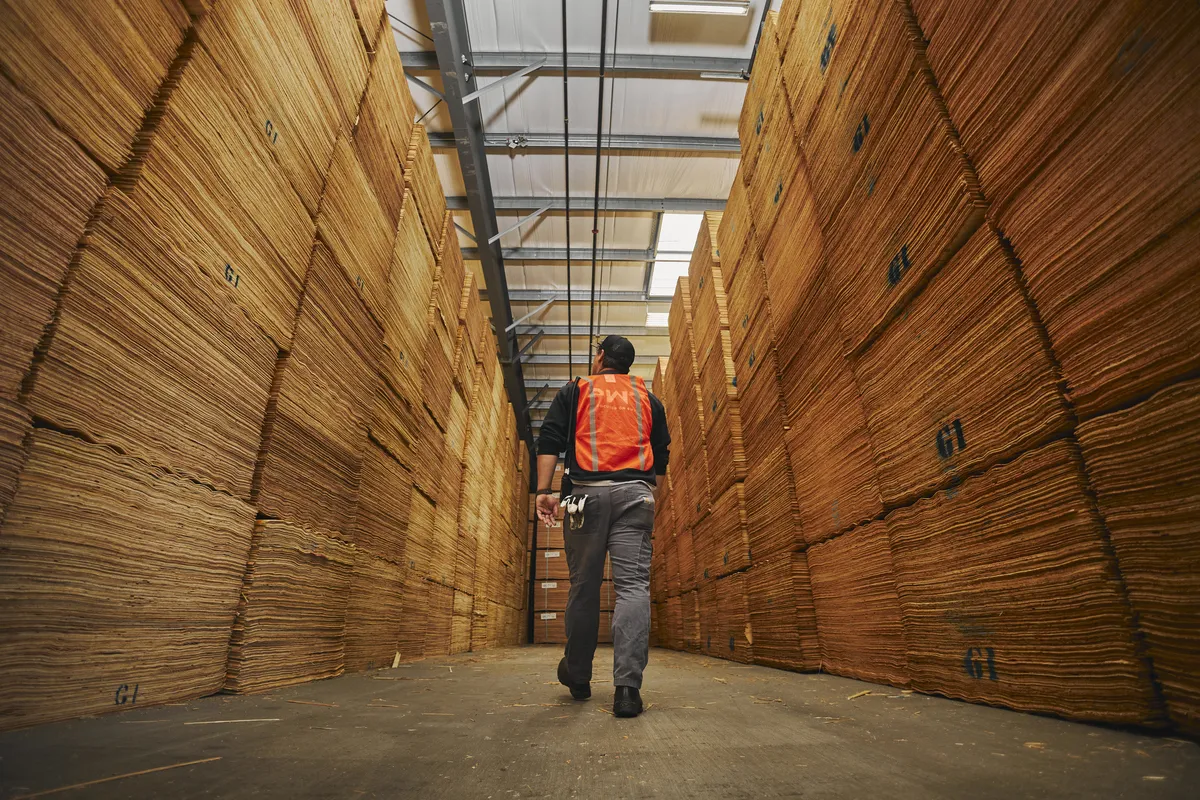 A worker walking between large stacks of PWT products in a warehouse.