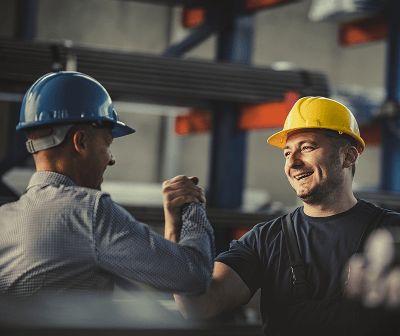 Two smiling workers in hard hats clasping fists together